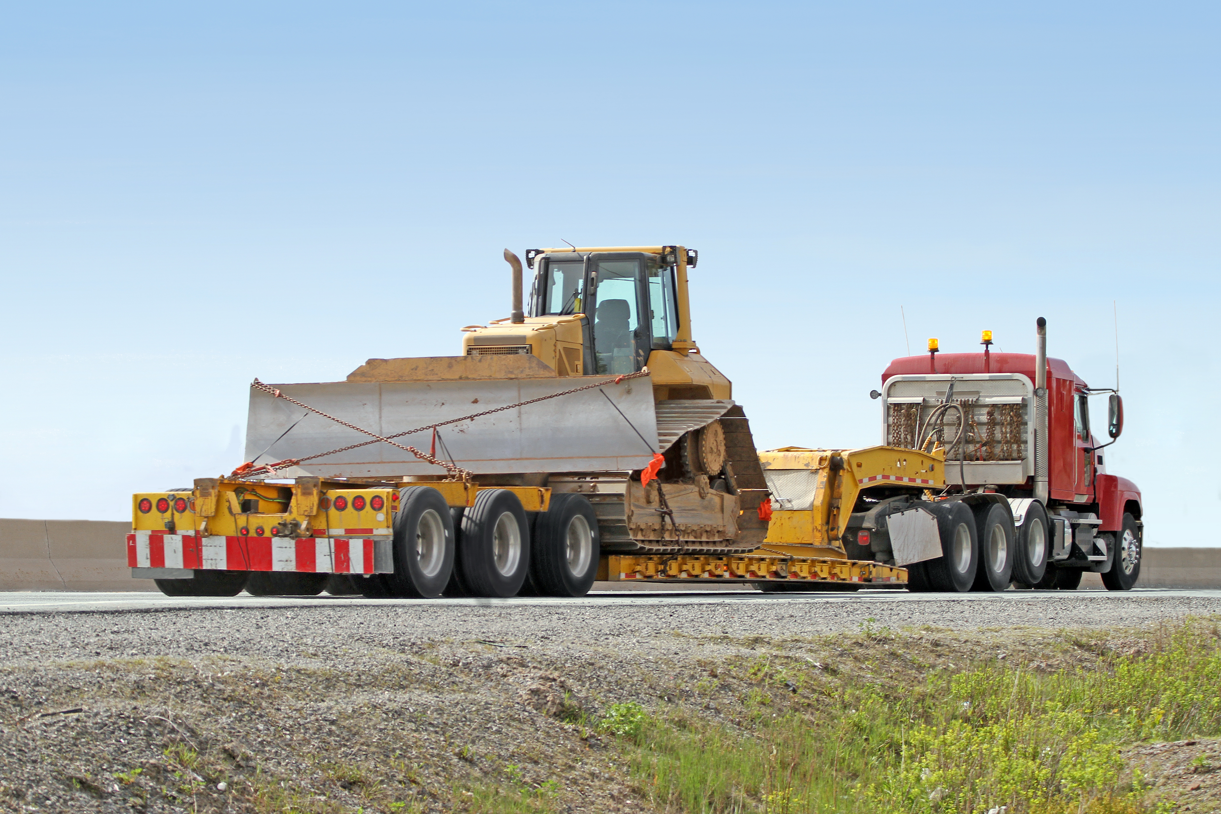 Rear quarter view of a flatbed semi truck on a highway transporting a large bulldozer.