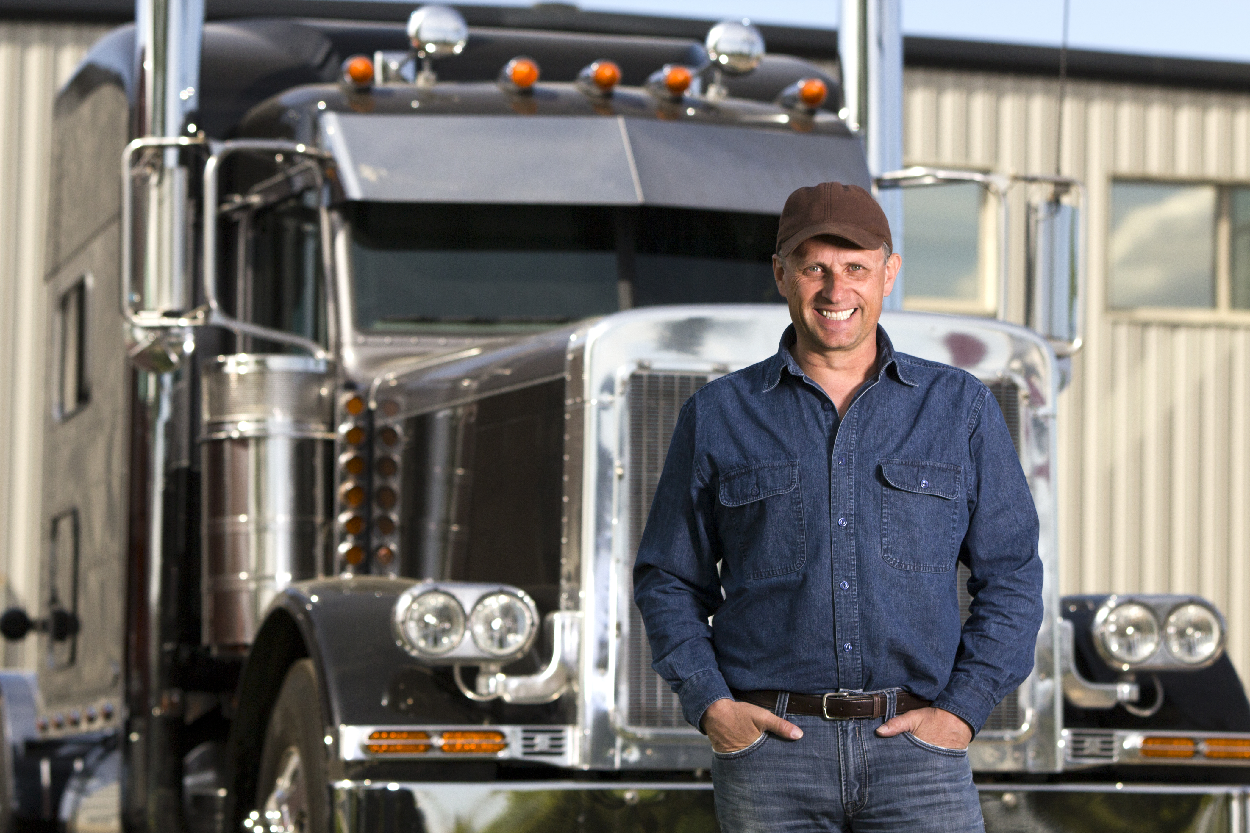 An image from the transportation industry of a truck driver in front of his truck at a distribution warehouse.
